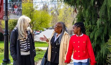 Three people walk along a path while talking with plants, grass and trees around them.