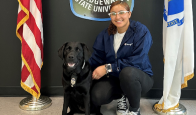 Alysiana Cruz wears a blue jacket and crouches down to pose next to a black K9 