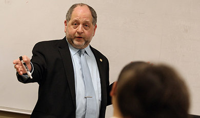 Aeon Skoble lectures in front of a white board while holding a marker.