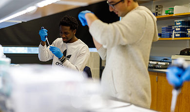 Two students use pipettes in a biology lab.