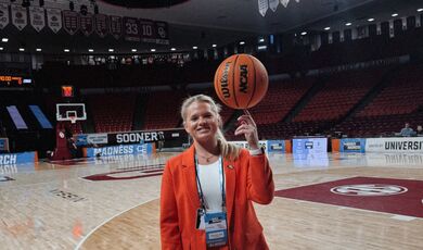 A woman wears a red suit and twirls a basketball on her finger 