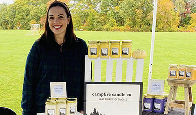 Ashley Twigg stands behind a display of her candles at an outdoor event.