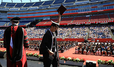 A graduate shows his diploma to the crowd while crossing the stage.