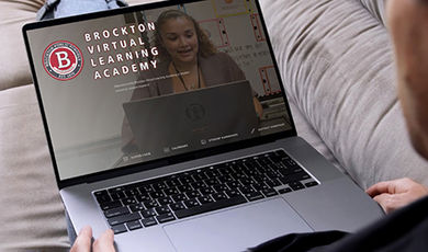 A person works on a laptop displaying the Brockton Virtual Learning Academy website.