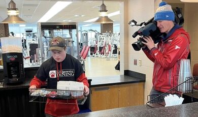 A videographer records a student working at a food stand.