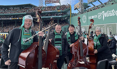 Bass players stand in front of the Green Monster and Fenway Park stands.