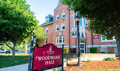 An exterior view of the front of Woodward Hall with a red sign displaying the hall's name in the foreground.