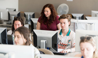 A class of students working at computers as their professor assists