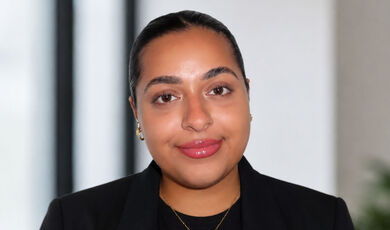 Zainab Al-Mosawi, '27, smiles with her dark hair entirely pulled back. She wears a black blazer over a black top.