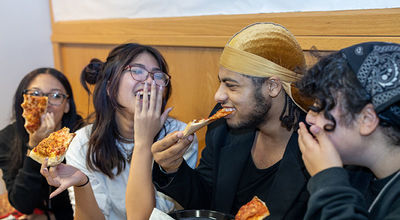 Four students laughing and eating pizza at a Pizza with the President event