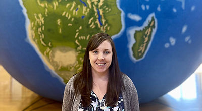 Courtney Sutcliffe stands in front of a giant globe.