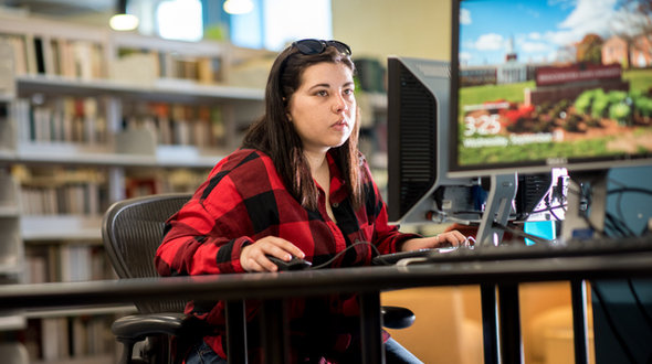 girl with long dark hair wearing red and black flannel shirt using a computer in Maxwell Library