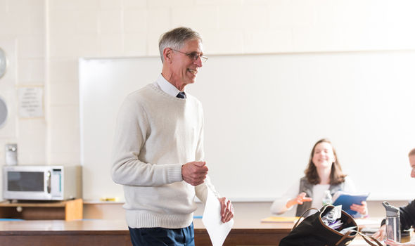 Dr. Steven Greenberg smiling and holding a piece of paper while teaching a class with a smiling female student sitting at a desk in background
