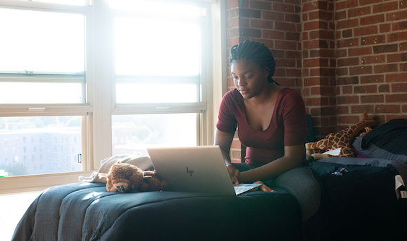 A student browses her laptop in her dorm