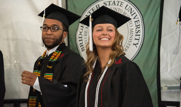 Two students smile while waiting to recieve their diplomas