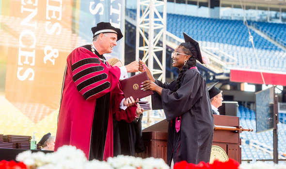 A BSU undergraduate accepts her degree from President Fred Clark with one hand and fist bumps him with the other