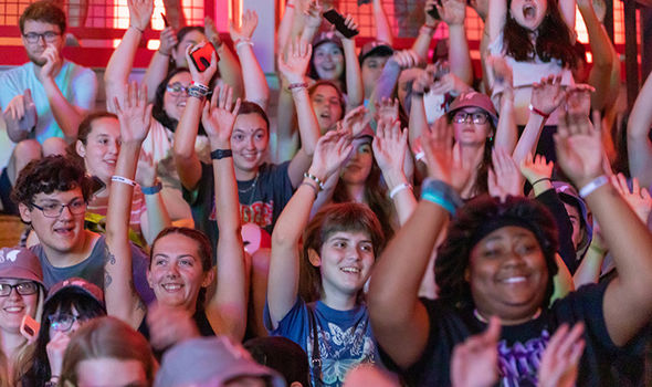 a large group of students sitting on bleachers with their hands in the air smiling and yelling