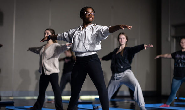 Students hold a yoga pose, with their arms outstretched