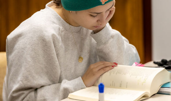 A student wearing a teal beanie studies an open book