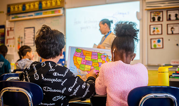 A BSU student teacher stands at front of an Elementary school classroom while 2 students work on a map of the United States