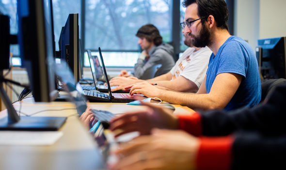 students sitting at a long table working on computers