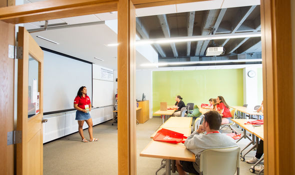 looking into a classroom where an orientation leader speaks in front of a white board while students sit at desks listening
