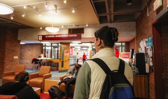 a BSU student walking toward the Academic Achievement Center entrance while other students sit in chairs and at tables outside the entrance
