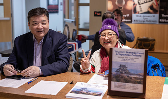 Two study abroad representatives smile for the camera; they have materials about studying in Japan on their table