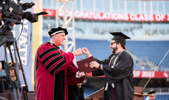 a male BSU student with short brown hair, beard and mustache fist bumps with BSU President Fred Clark as he crosses the Commencement stage and receives his degree
