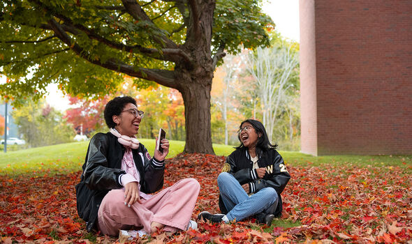 Two students sitting among red leaves under a tree on BSU's campus