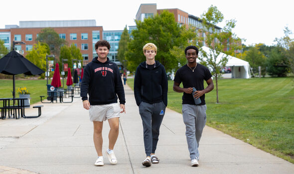 3 male students smile while walking together through University Park
