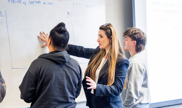 Dr. Albulene Kastrati standing in front of a white board with students showing them how to do something on the board