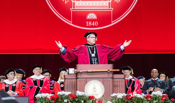 President Fred Clark speaking at the podium on stage at Commencement gestures with his arms open and palms up