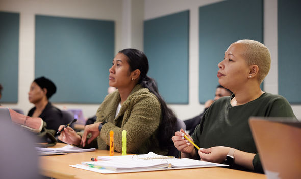 3 students sit at tables listening to their professor