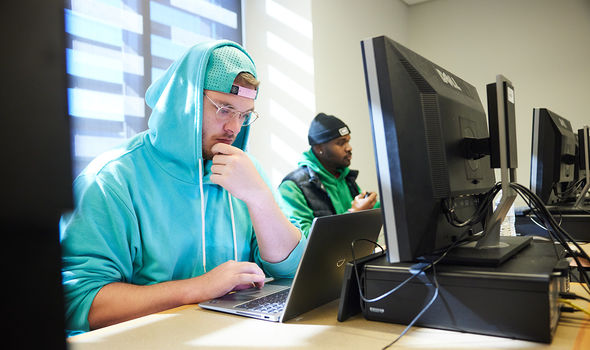 Two students working on laptops and computer workstations in a cybersecurity class
