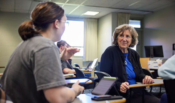 Dr. Pamela Myette sitting in a classroom desk talking to a student in class