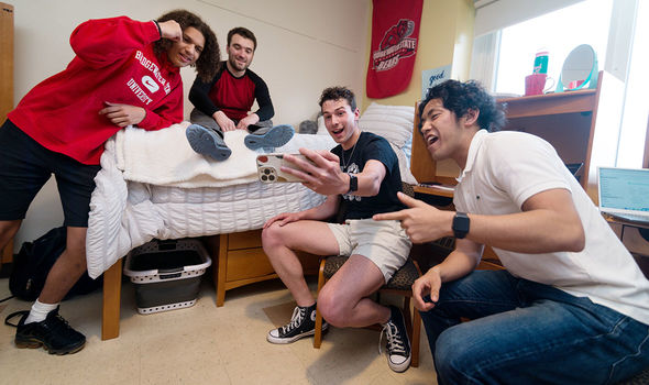 Four students laughing and looking at a phone in a BSU dorm room