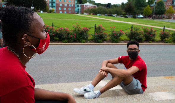 Two students in masks sitting on the steps of Boyden Hall