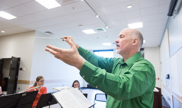 Dr. Donald Running directing flute players who are seated behind music stanchions