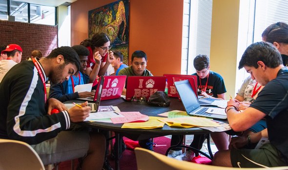 students around a table with laptops open and an Orientation Leader helping them