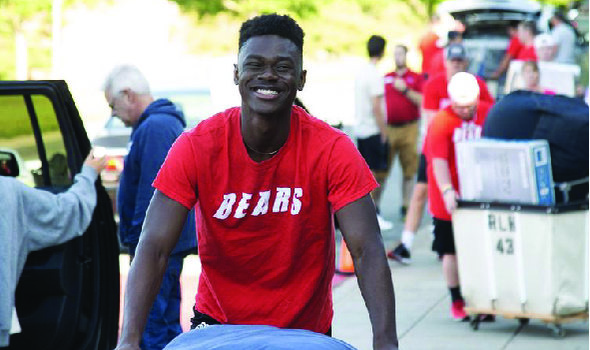 smiling student wearing a 'Bears' shirt pushing a bin on move in day