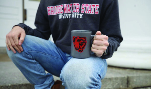 kneeling with a Bridgewater state bear logo mug and a Bridgewater state university sweatshirt