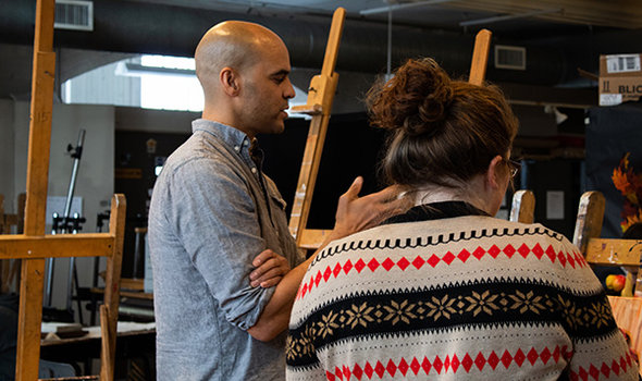 Visiting faculty member talking to a student about a painting on an easel in art studio