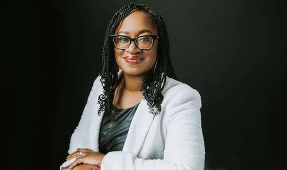 Dr. Keisha Blain looks straight ahead smiling in black glasses and a light grey blazer. Her hair is in braids.