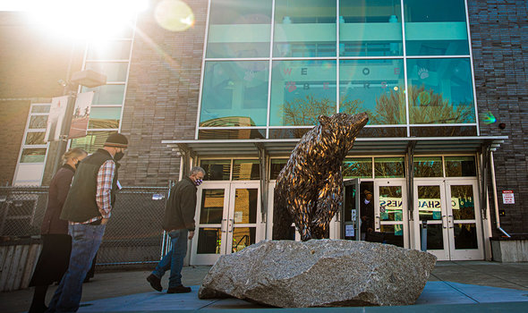 Three people walking near the bronze bear sculpture