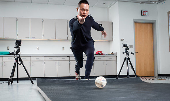 a student "bowling" a ball in lab while being recorded with small balls attached to his clothing