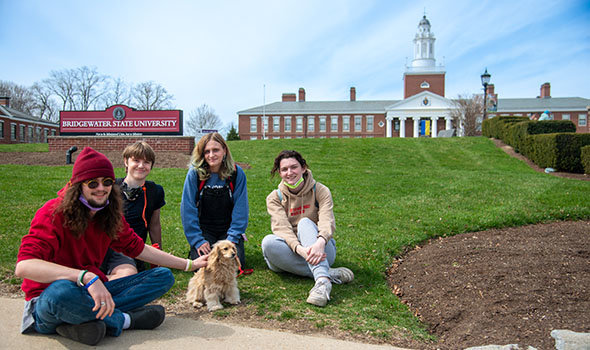 Four students sitting in front of the BSU sign with a cute little dog