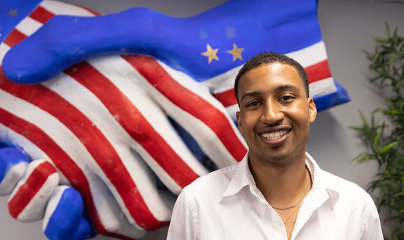 Student Mariojardel Centeio smiling in front of a sculpture of two hands shaking — one hand is painted with the flag of Cape Verde and the other is painted with the flag of the US