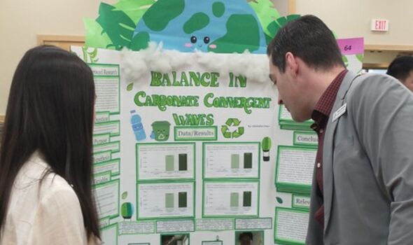 A BSU professor looking at a student's science fair display on recycling