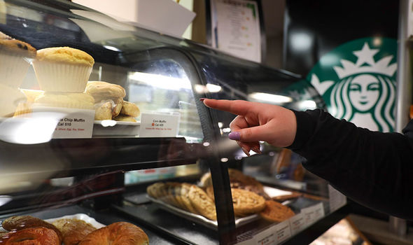 A finger points to a bakery item in a display, with the Starbucks logo in the background